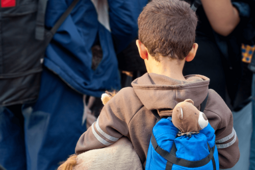 A young child with a backpack and cuddly toys